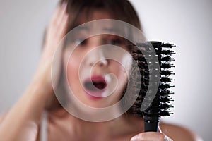 Young Woman In Bathrobe Holding Comb Looking At Hair Loss