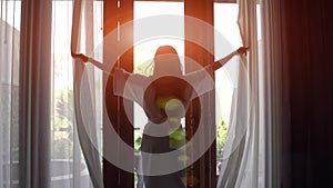 Young woman in bathrobe open curtains and stretch standing near the window at home.