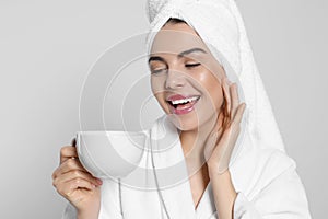 Young woman in bathrobe with towel and cup of drink on light grey background. Spa treatment