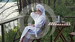 Young woman in a bathrobe and towel on the terrace on a background of mountains and forest. woman with a cup of tea and