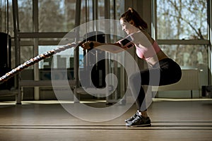 Young woman with battle ropes exercise in the fitness gym