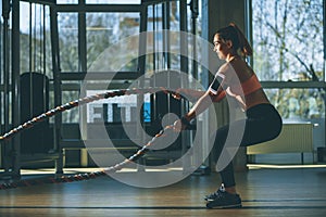 Young woman with battle ropes exercise in the fitness gym