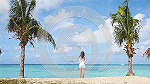 Young woman on the beach during caribbean vacation. Adorable lady standing between palm trees on Antigua island