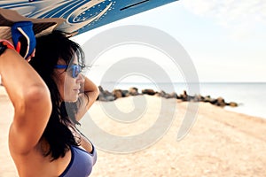 Young woman on the beach carries a surfboard on her head