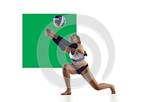 Young woman, beach volleyball player in motion during game, hitting ball over white background with green element.