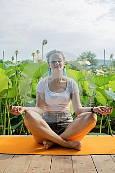 young woman with beautiful blue dreadlocks resting on yoga mat on lotus lake