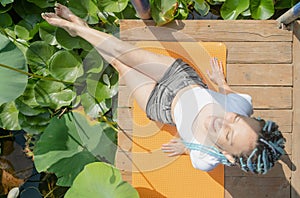 young woman with beautiful blue dreadlocks resting on yoga mat on lotus lake