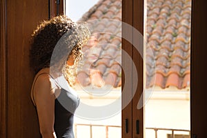 Young woman, beautiful, brunette, with curly hair, in a black dress, looking absentmindedly out the window of a room in a