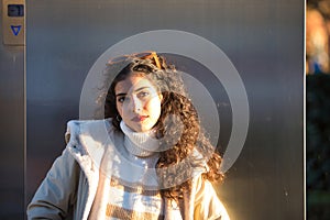 Young woman, beautiful, brunette with curly hair, sweater, coat and sunglasses, leaning on a metal wall, sensual and flirtatious