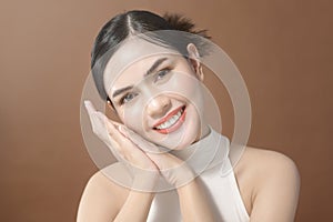 Young woman with beautiful face smiling , touching her face over brown background , beauty skin care concept