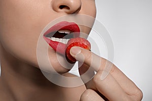 Young woman with beautiful lips makeup eating strawberry on light background, closeup