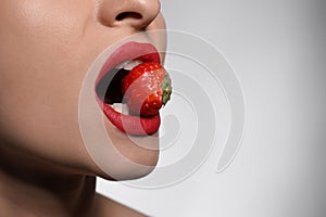 Young woman with beautiful lips makeup eating strawberry on light background, closeup. Space for text