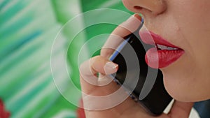 Young woman with beautiful lips talking on the phone on the blurred green leaves background