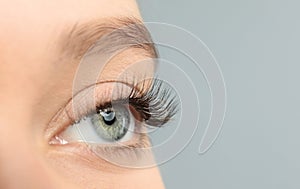 Young woman with beautiful long eyelashes on gray background, closeup