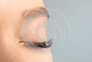 Young woman with beautiful long eyelashes on gray background, closeup.