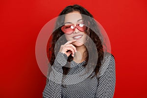 Young woman beautiful portrait, posing on red background, long curly hair, sunglasses in heart shape, glamour concept