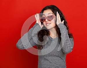 Young woman beautiful portrait, posing on red background, long curly hair, sunglasses in heart shape, glamour concept