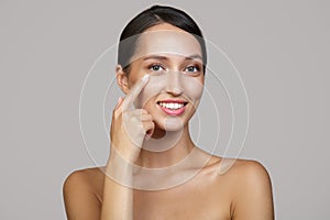 A young woman with a beautiful smile and teeth points her finger at her eyes. Caring for the skin. Copycpase