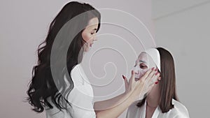 Young woman in beauty cosmetology salon with a cloth mask on face talks with female doctor dermatologist