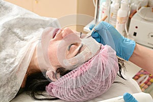 Young woman in beauty salon does make application of moisturizing, softening, regenerating mask