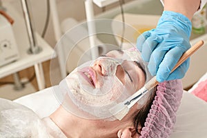 Young woman in beauty salon does make application of moisturizing, softening, regenerating mask