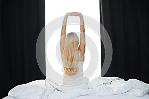 Young woman in the bed. Beautiful blond girl wakes up. Morning in the bedroom, daylight from the window. Health and rest