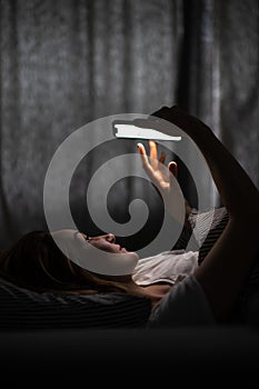 Young woman in bed holding a phone,