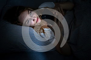 Young woman in bed holding a phone, tired and exhausted,