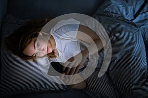 Young woman in bed holding a phone, tired and exhausted, blue light straining her eyes