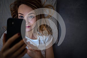 Young woman in bed holding a phone, tired and exhausted, blue light straining her eyes