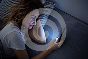 Young woman in bed holding a phone, tired and exhausted, blue light straining her eyes photo