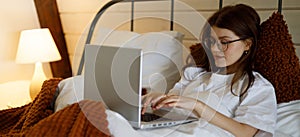 Young woman in bed with laptop, lazy leisure time at home