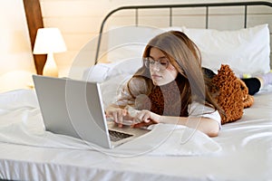 Young woman in bed with laptop. Work and leisure in a cozy home interior