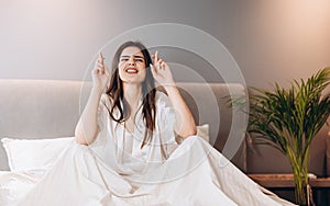 young woman in bed in white pajamas crossed her fingers for luck. In the morning or evening before an important event