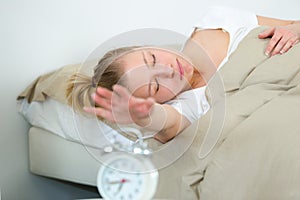 young woman on bed yawn awakening tired holding alarm clock