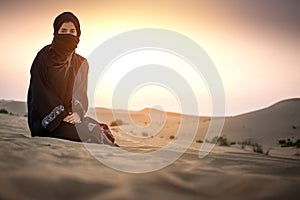 Young woman Bedouin in black traditional clothes against sunset sky over desert.