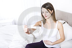 Young woman in bedroom at home wearing in white check pregnant test