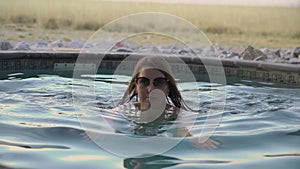 A young woman in a beige bikini bathe a private swimming pool.