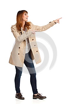 Young Woman In Beige Coat Is Standing, Pointing And Laughing