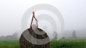 Young woman in beige dress lying on haystacks at twilight time