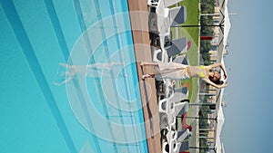 Young woman in beige pareo resting by poolside, silhouette reflected in water