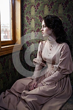 Young woman in beige vintage dress of early 20th century sitting