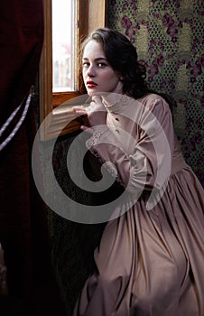 Young woman in beige vintage dress of early 20th century sitting