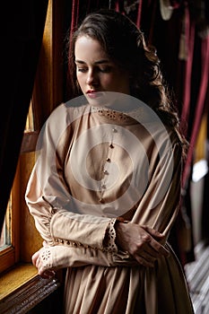 Young woman in beige vintage dress of early 20th century standin