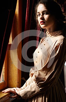 Young woman in beige vintage dress of early 20th century standin