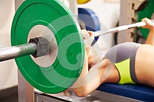 Young woman bench pressing weights at gym, focus on barbells