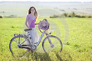 Young woman with a bicycle on green field on a sunny day