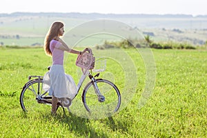 Young woman with a bicycle on green field on a sunny day