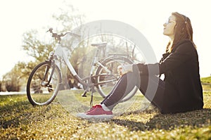 Young woman with bicycle relaxing sitting on grass in nature park