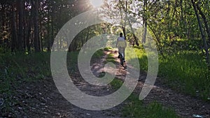 Young Woman on a Bicycle Rides Along Green Forest Path in Sunny Summer Day